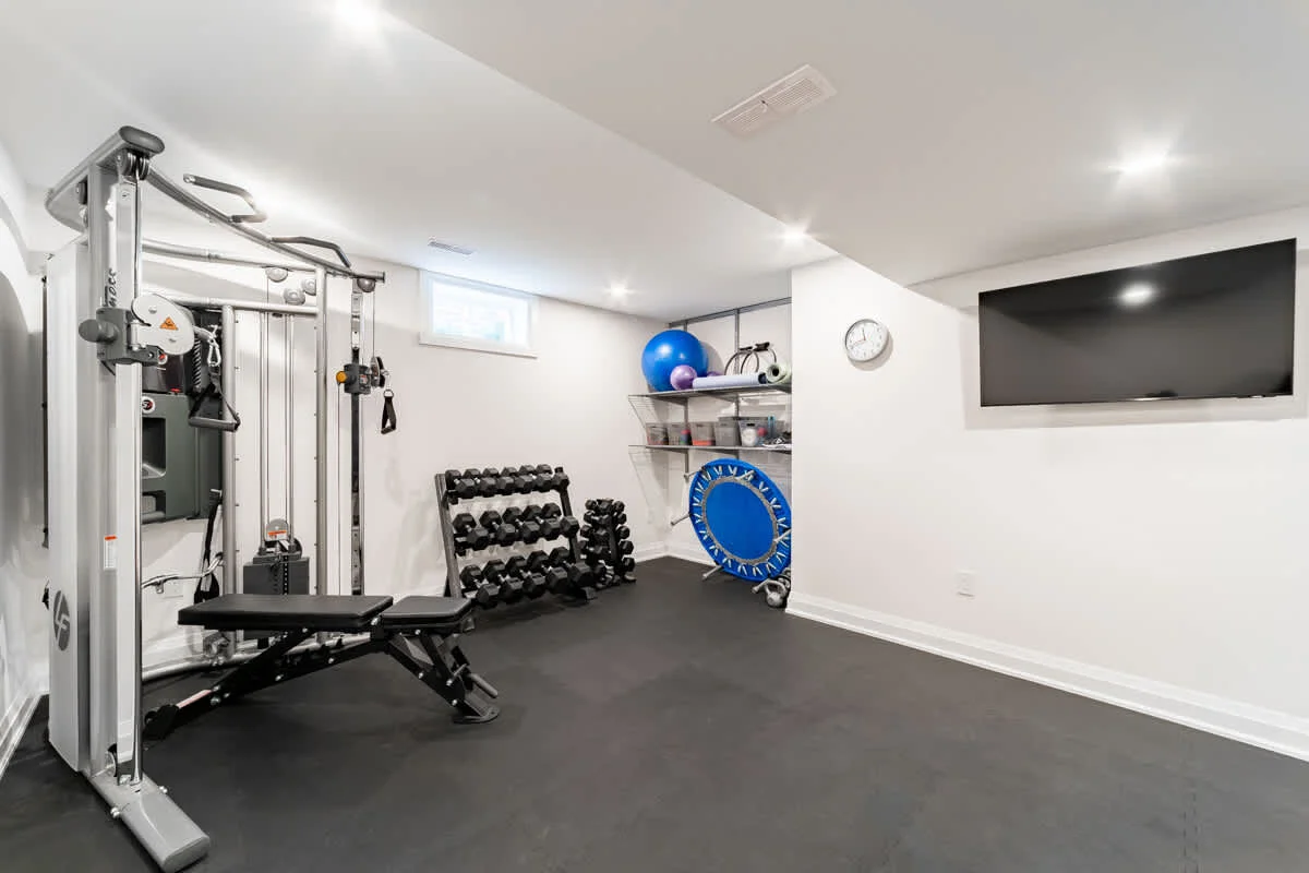 Renovated basement gym with exercise equipment, dumbbells, and wall-mounted TV