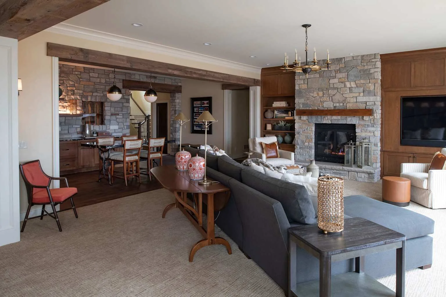 Rustic basement entertainment room with L-shaped sofa, stone fireplace, and built-in wet bar