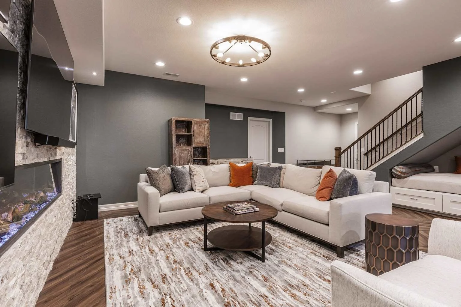 Modern finished basement with L-shaped sofa, gas fireplace, mounted TV, and built-in cabinets